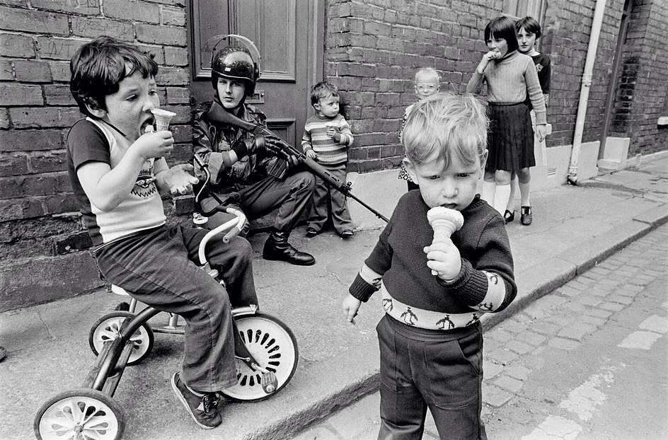 Children eating their ice creams while soldiers patrol the streets of Londonderry. Ten years after the arrival of British troops in the province. Londonderry. Northern Ireland. G.B. 1979. Peter Marlow Foundation - Magnum Photos.jpg